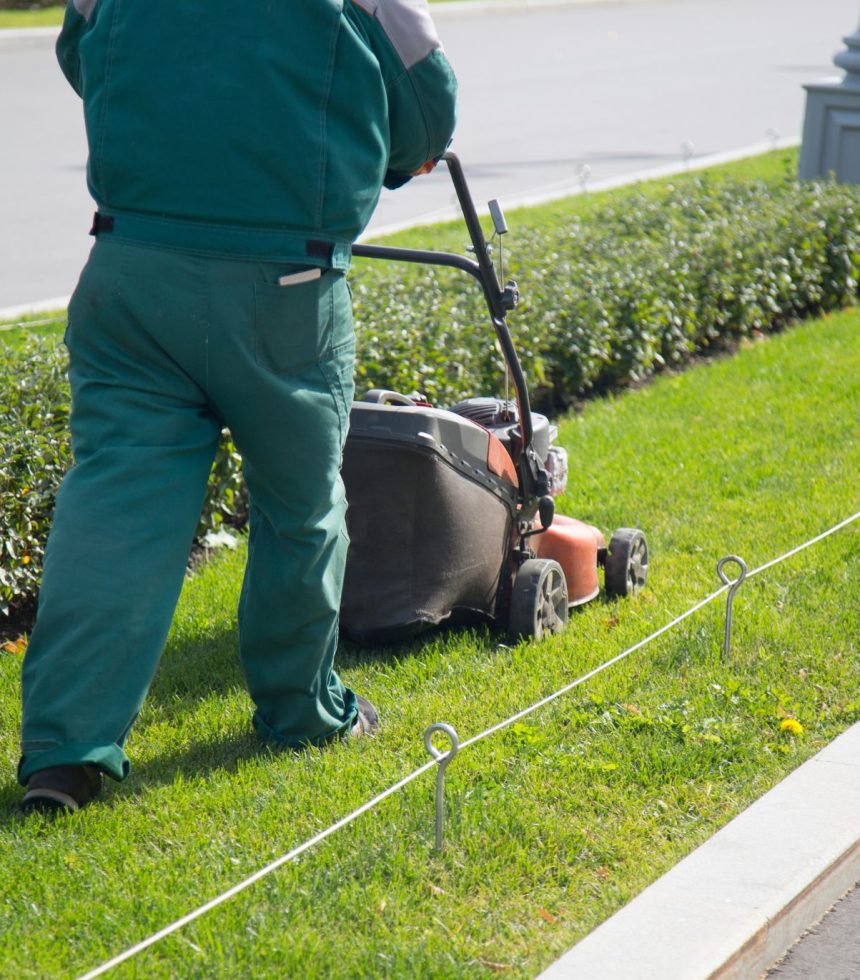 A man in a green uniform mowing grass as part of a lawn care service in Bellevue, WA.